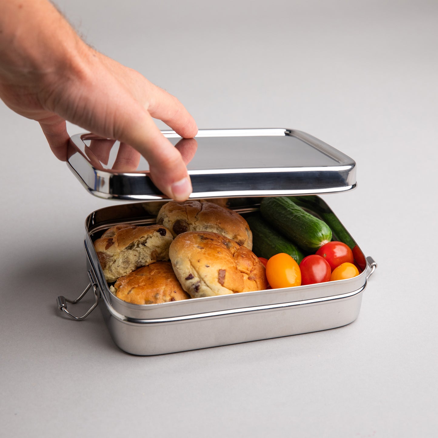 RVS lunchbox die word geopend door een hand. rijkelijk gevuld met een gezonde lunch