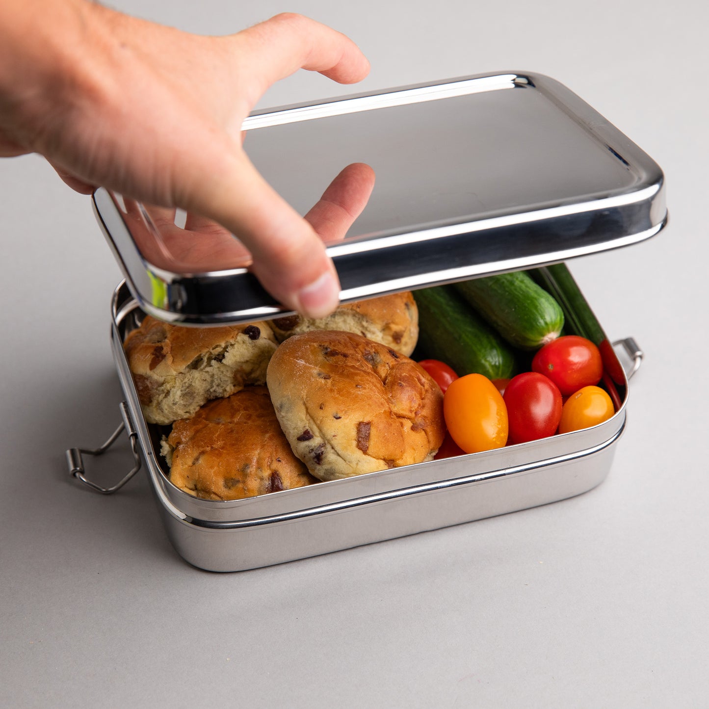grote RVS lunchbox die wordt geopend door een hand, gevuld met lunch