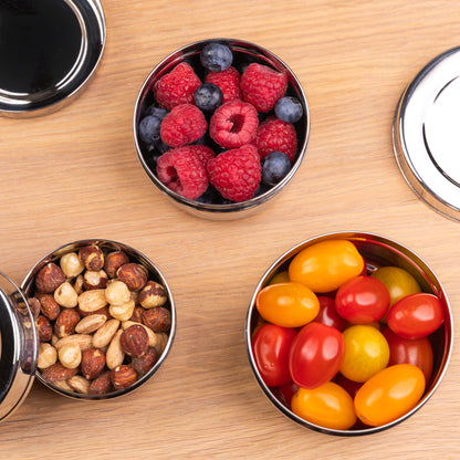 3 RVS snackboxen gevuld met fruit op een schooltafel