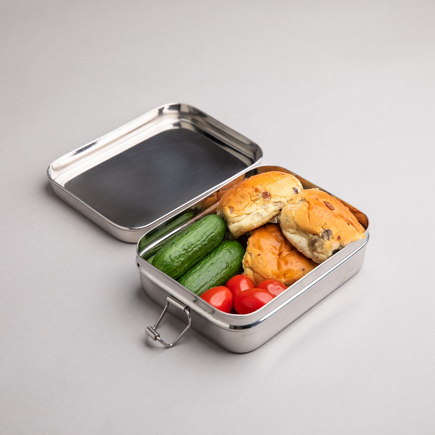 kleine RVS lunchbox gevuld met krentebollen, komkommer en tomaat