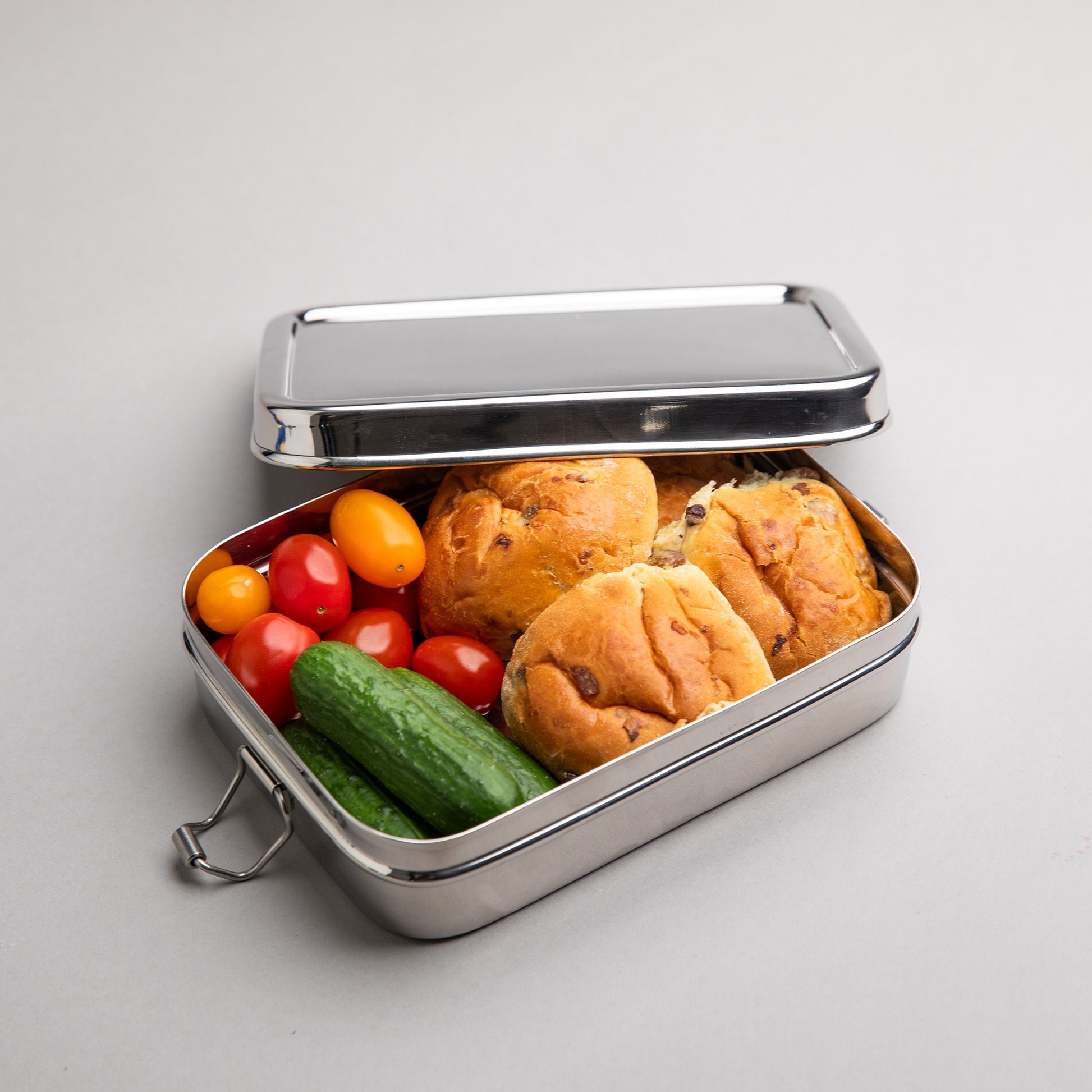 RVS lunchbox geopend en gevuld met krentebollen en tomaat